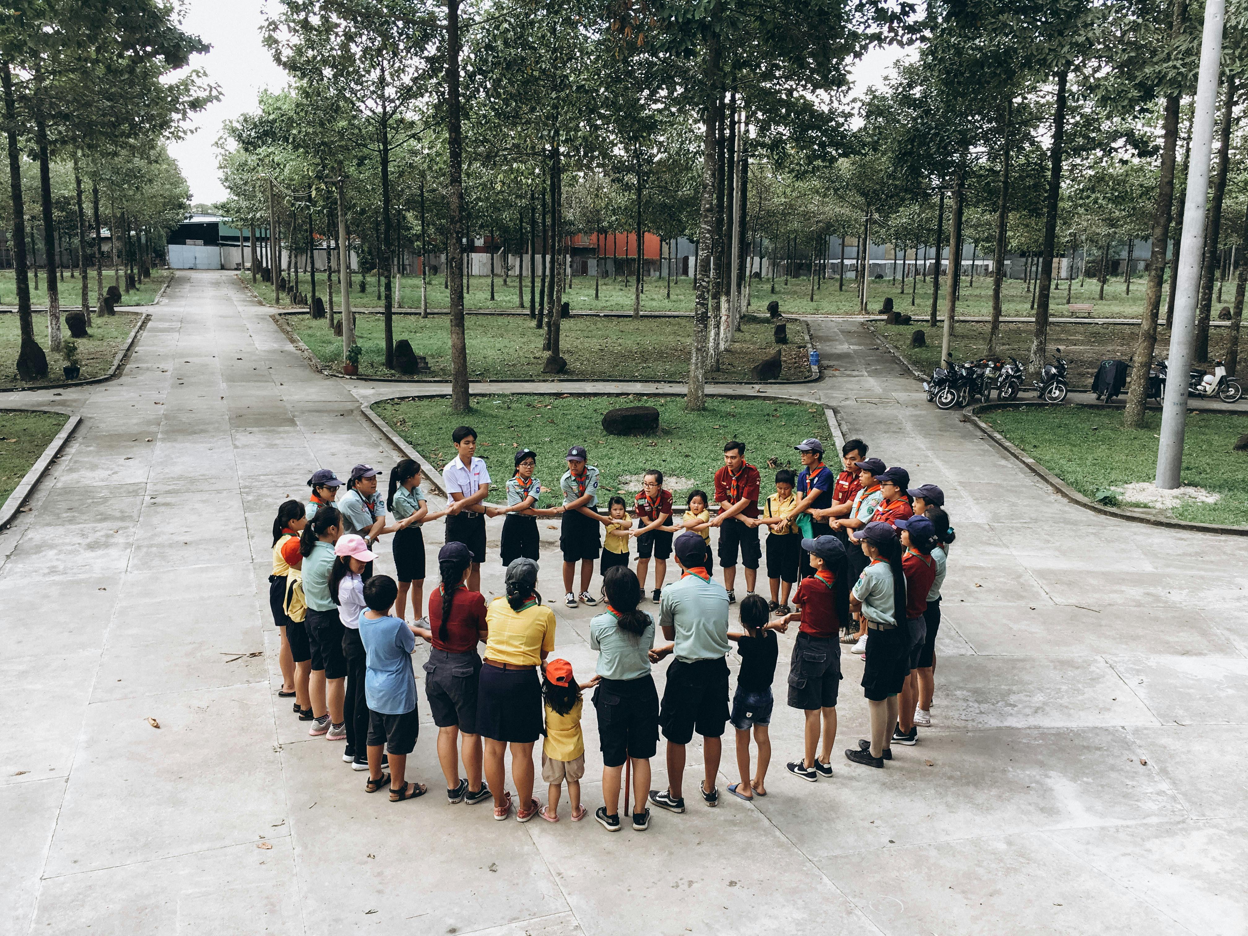 Group of people engaging in a team-building exercise outdoors, forming a circle in a park setting.