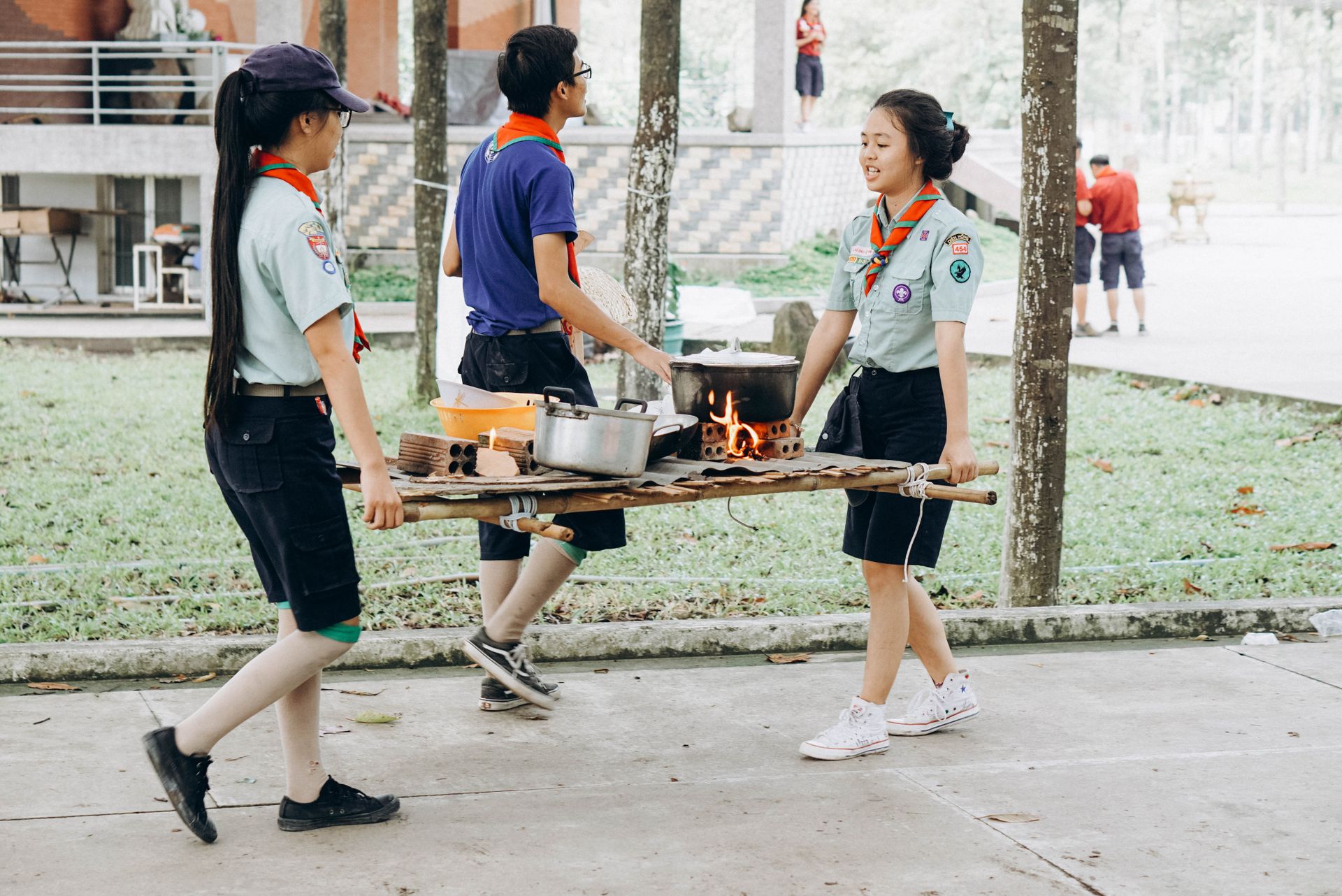 Youth scouts engaging in an outdoor cooking activity, carrying food and pots.