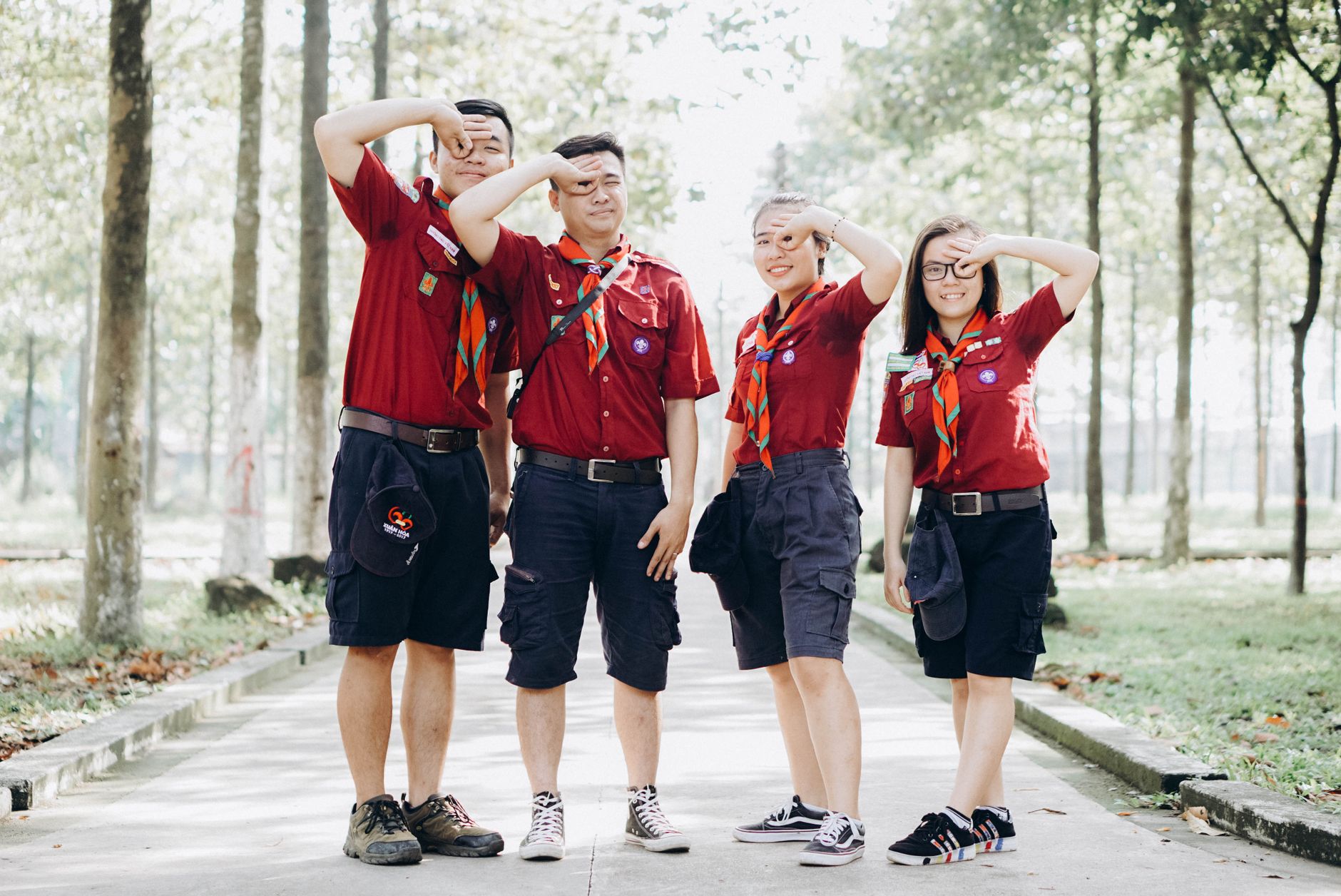 Four young scouts in uniform salute confidently while standing on a sunny pathway.