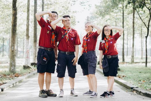 Four young scouts in uniform salute confidently while standing on a sunny pathway.