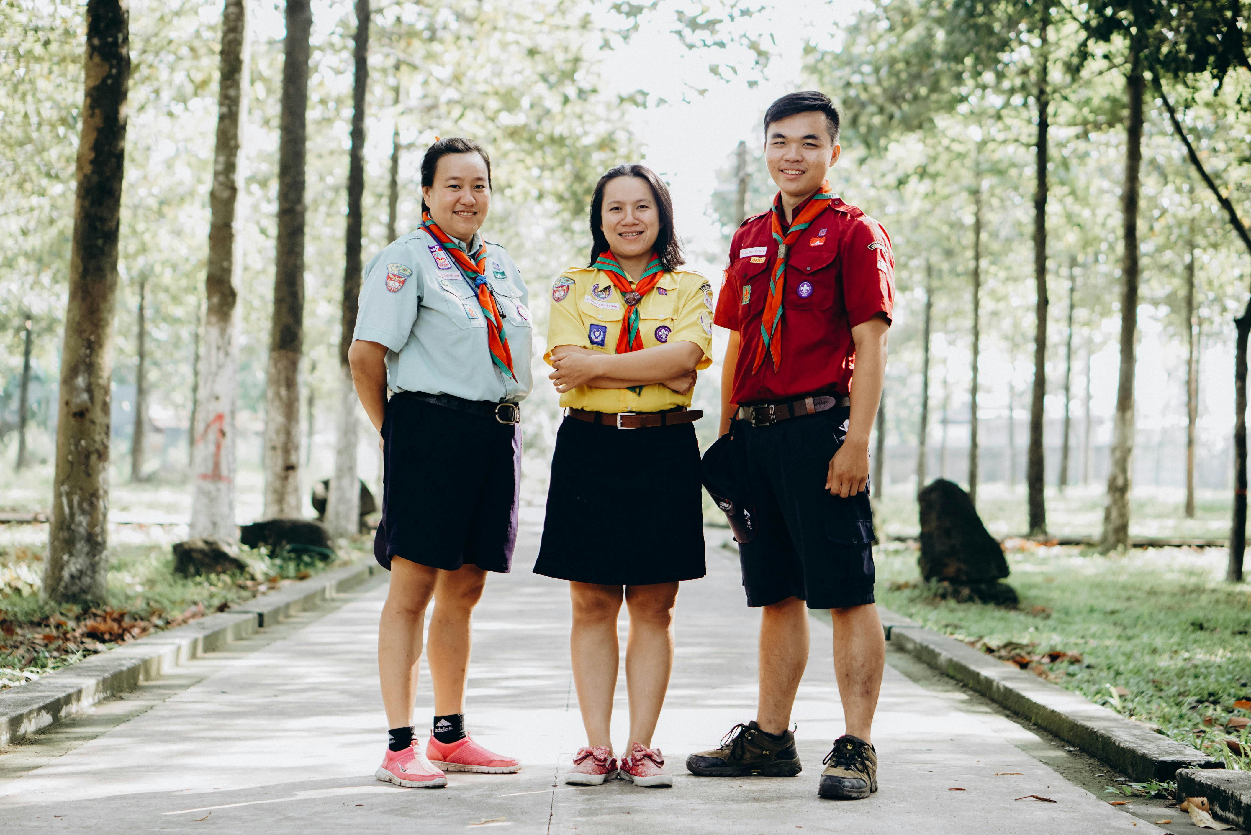 Three adult scouts in uniform pose for a photo in a park setting, showcasing teamwork and unity.