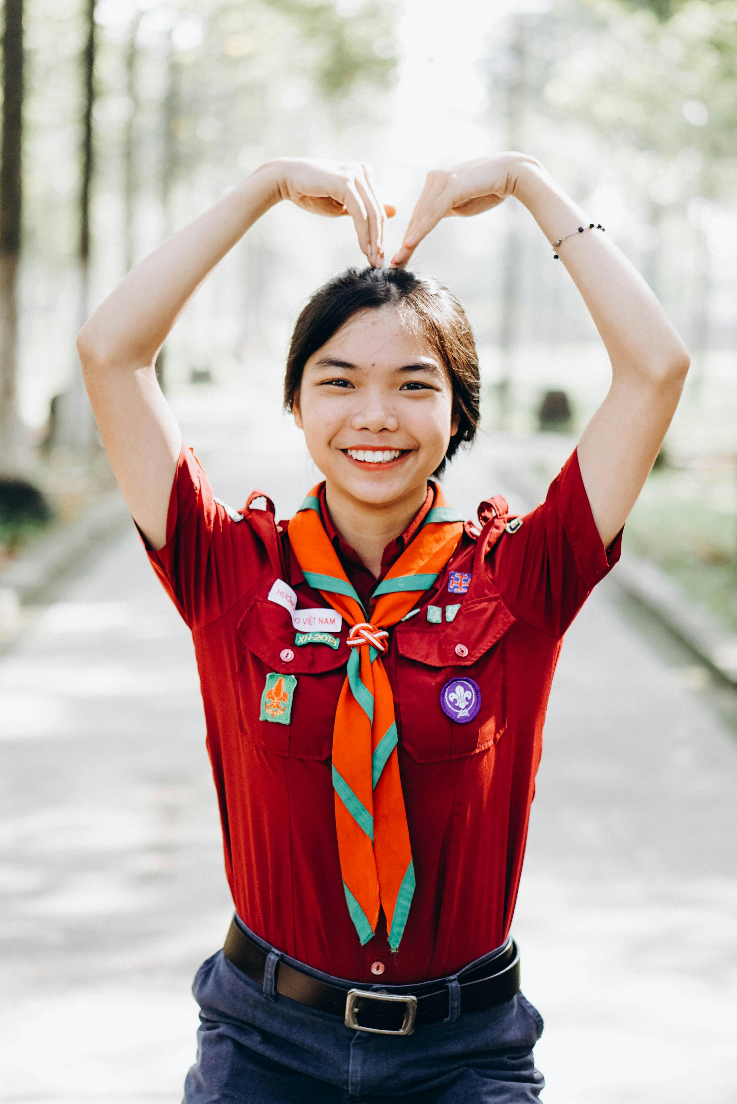 Smiling scout member making heart shape with hands outdoors.