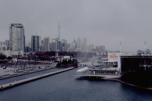 Overcast view of Toronto skyline with prominent CN Tower, illustrating urban landscape by waterfront.