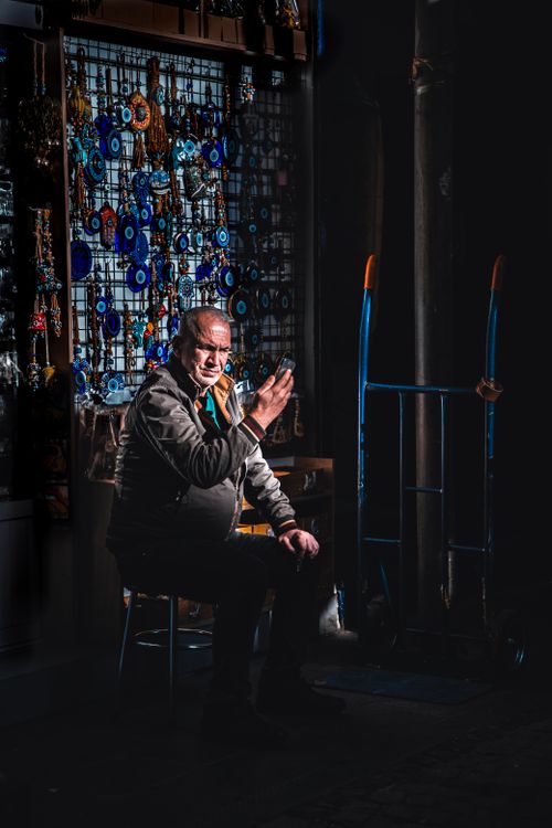 Free Man sitting by evil eye trinkets in a dimly lit shop in Istanbul, Turkey. Stock Photo