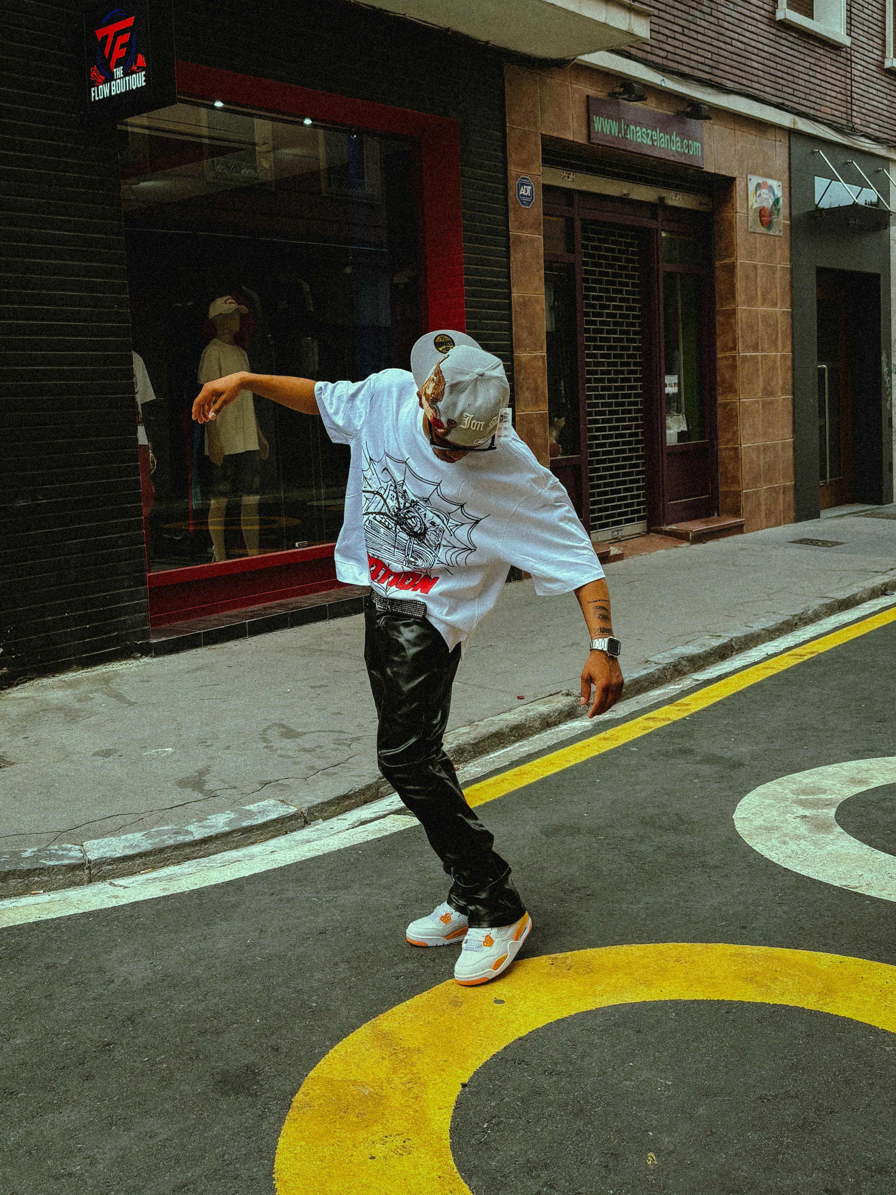 Young man in stylish outfit dancing on urban street with vibrant graffiti.