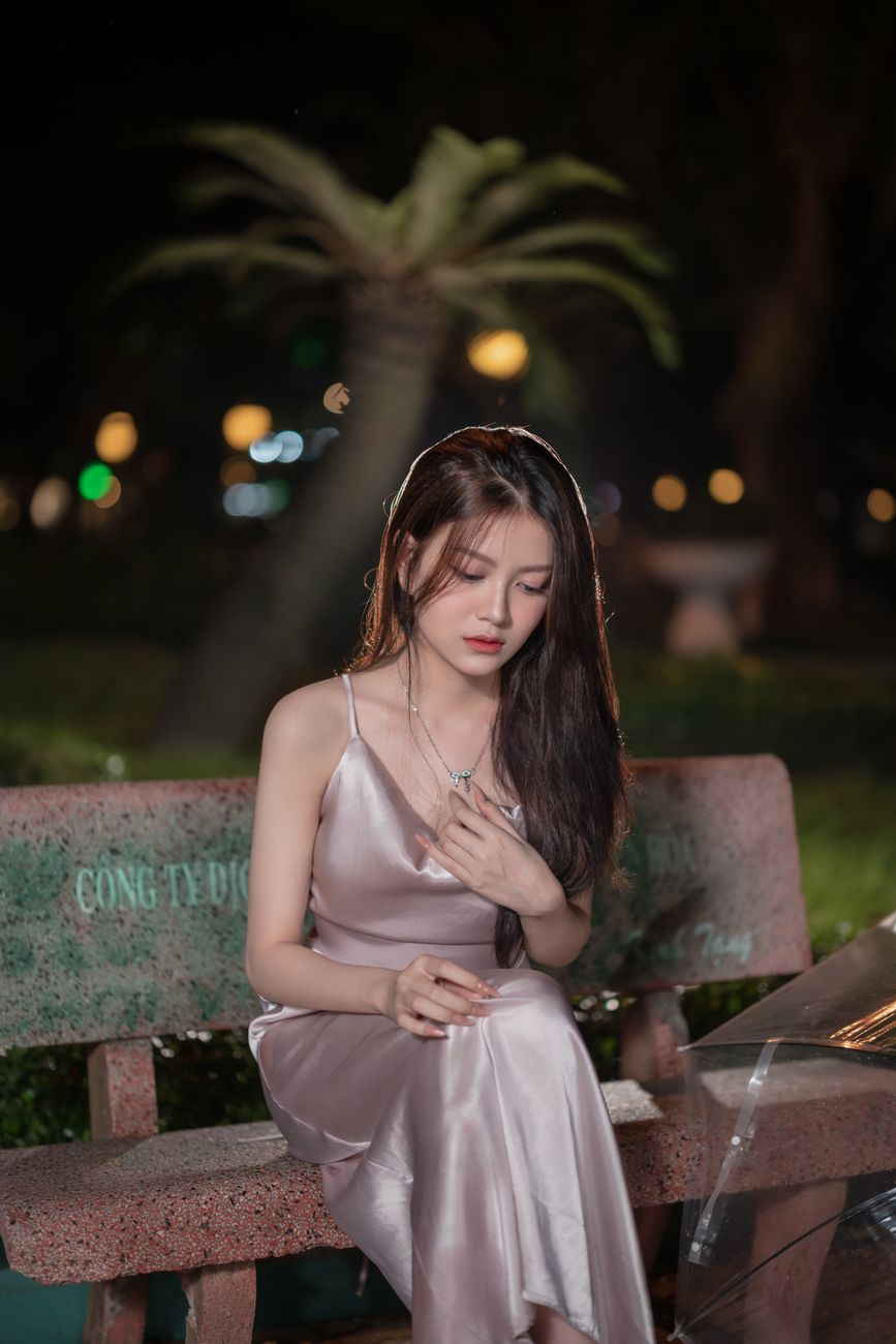 Captivating portrait of a woman in a silky dress on a park bench at night, exuding elegance and tranquility.