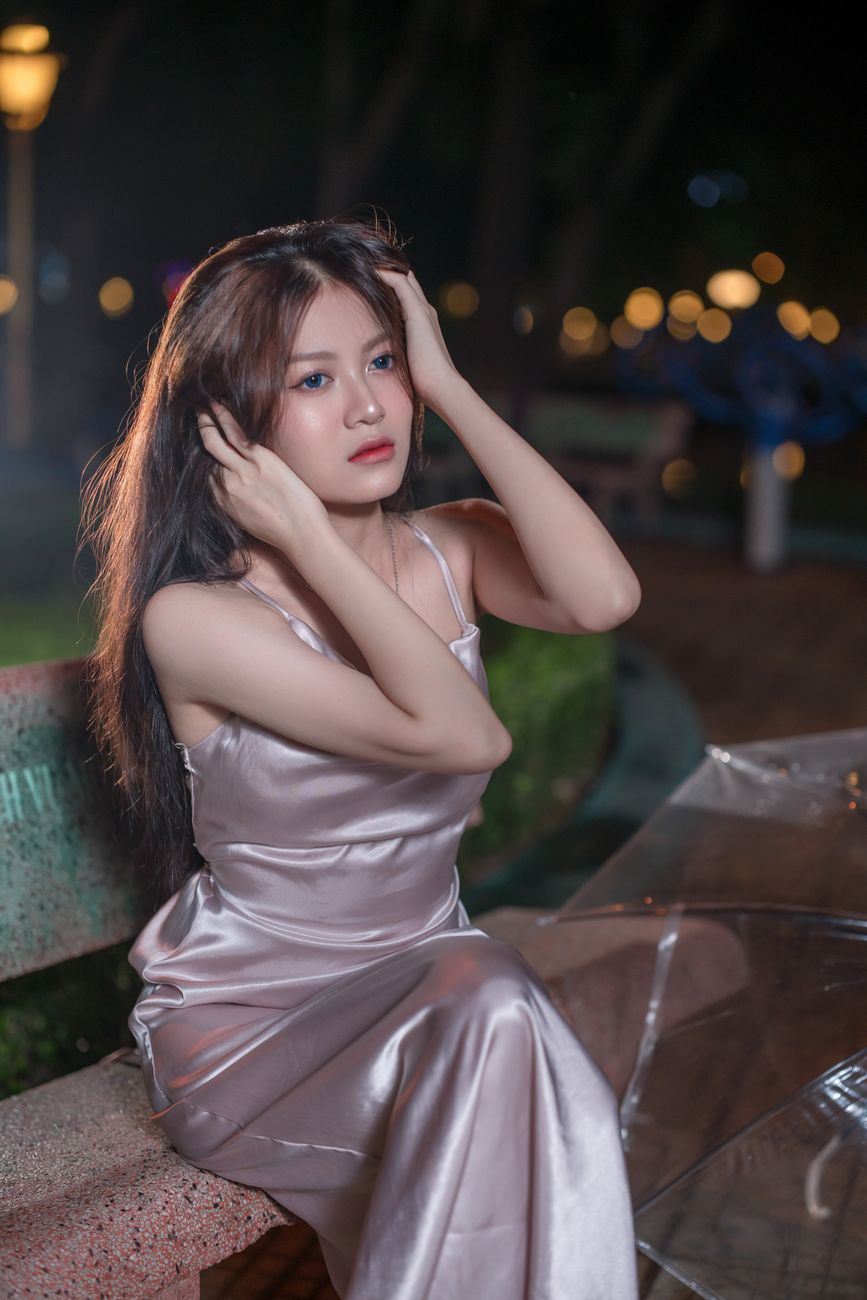 A woman in an elegant gown poses thoughtfully in a park at night.