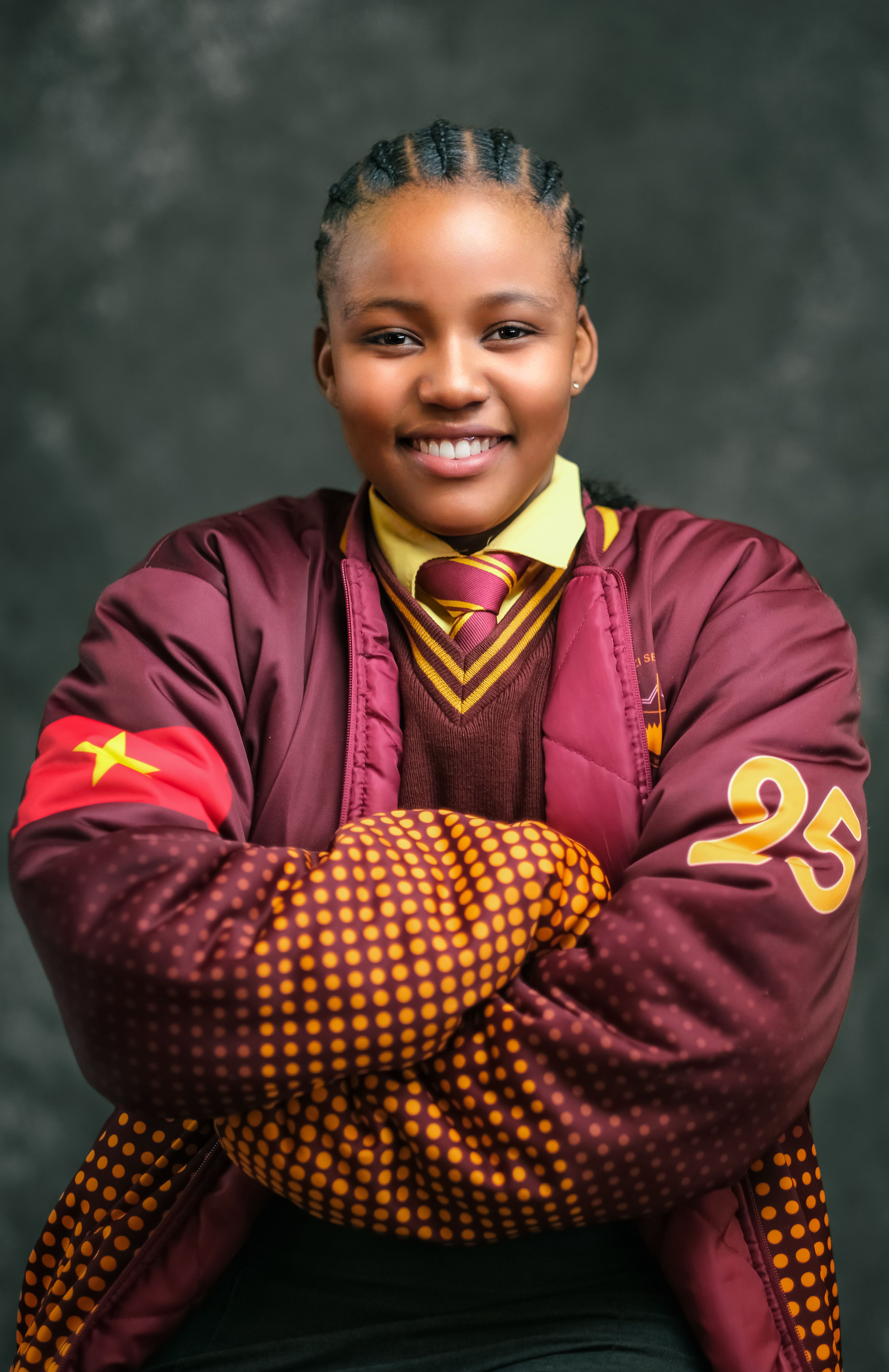 Portrait of a smiling teenager in a burgundy jacket with yellow accents.