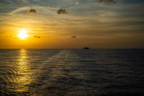 Free Beautiful sunset over the ocean with a ship silhouette on the horizon. Stock Photo