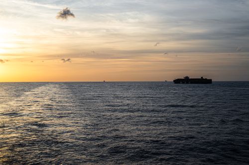 Free A serene cargo ship sails on a tranquil ocean during sunset with vibrant sky hues. Stock Photo