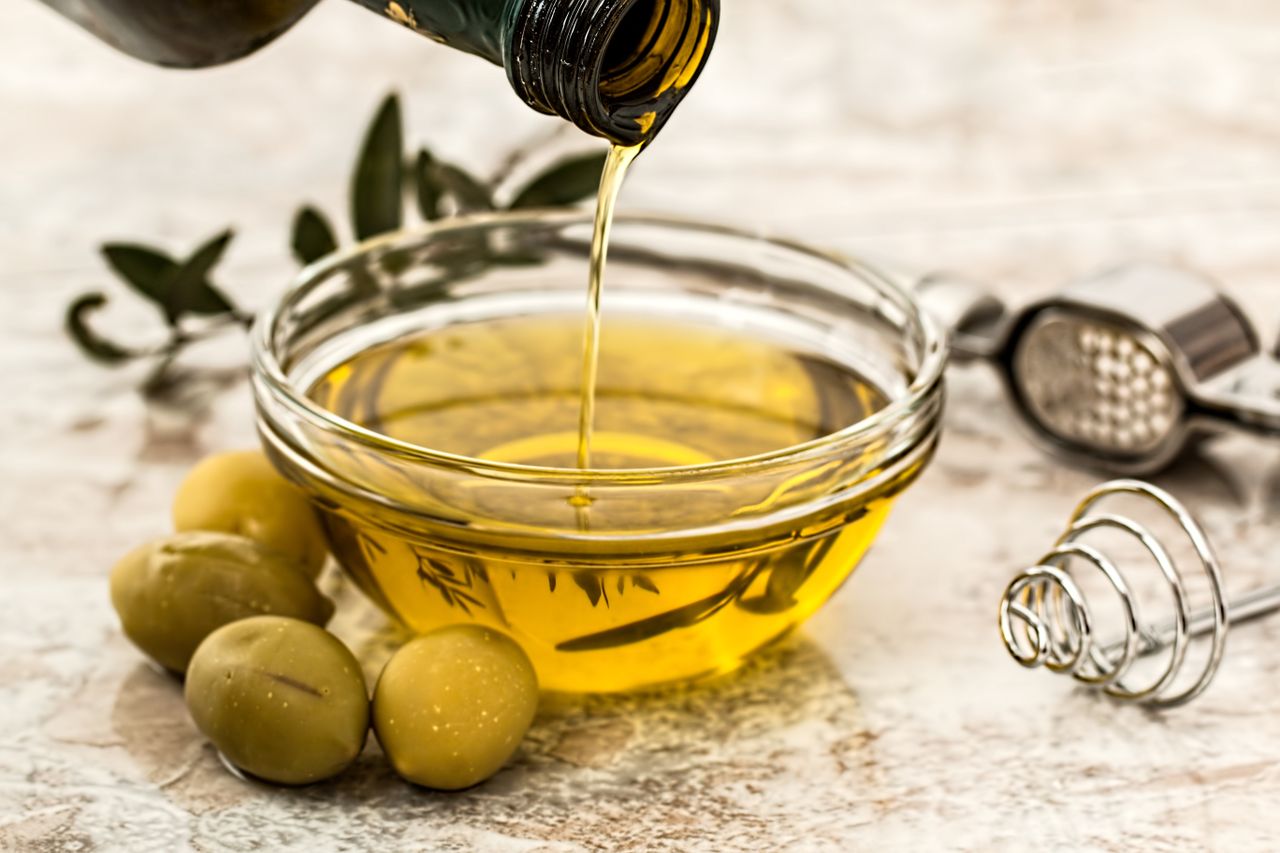 Olive oil being poured into a glass bowl beside fresh olives