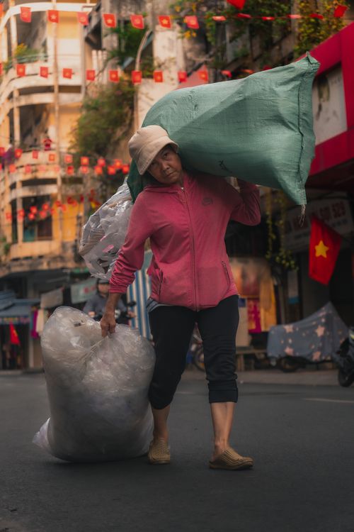 Free A dedicated worker hauling heavy bags on a bustling street adorned with flags and vibrant colors. Stock Photo