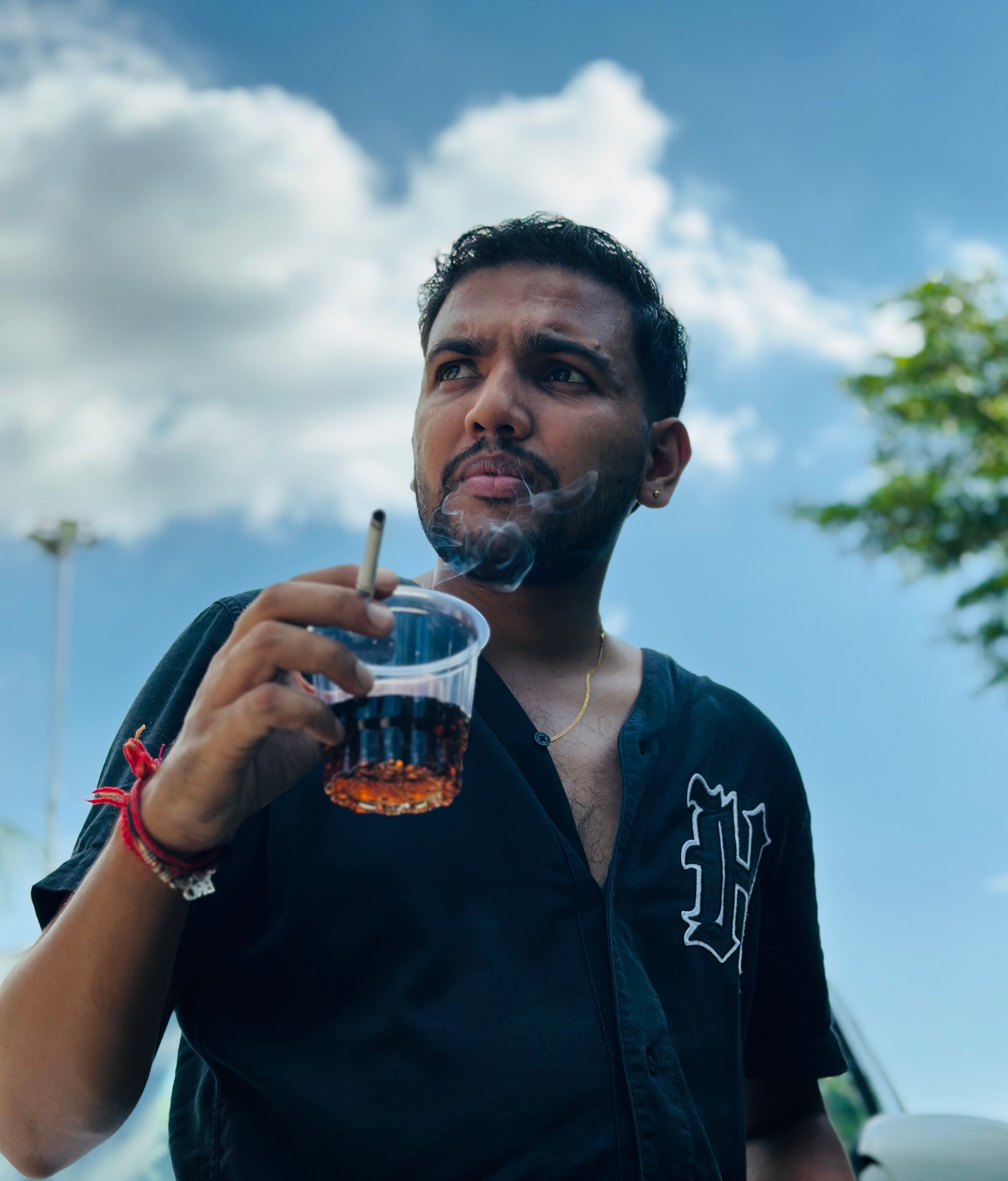 Adult male enjoys a drink and cigarette outdoors in sunny Phagwara, India.