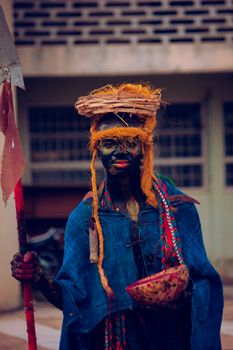 Person in traditional African attire with face paint and headpiece, holding spear