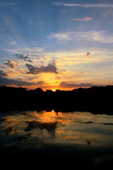 Beautiful sunset with vibrant colors reflecting on a serene river, surrounded by silhouette of trees.