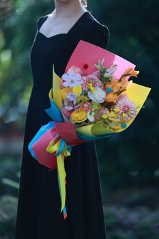 Woman in black dress holds vibrant flower bouquet outdoors.