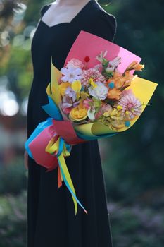 Close-up of a floral bouquet held by a woman in elegant attire, featuring vibrant colors.