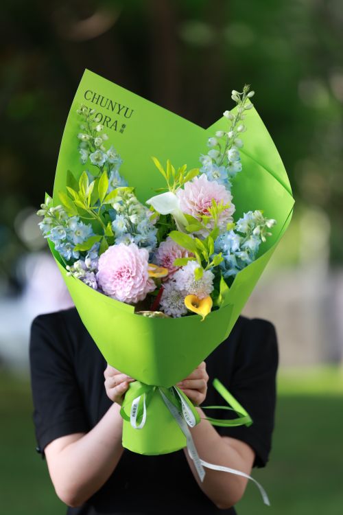 Free A variety of colorful flowers beautifully arranged in a green wrapper held by a person. Stock Photo