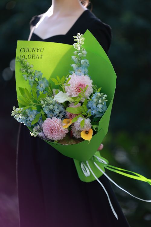 Free A woman holds a vibrant bouquet of various flowers in a green wrapping outdoors, conveying elegance. Stock Photo