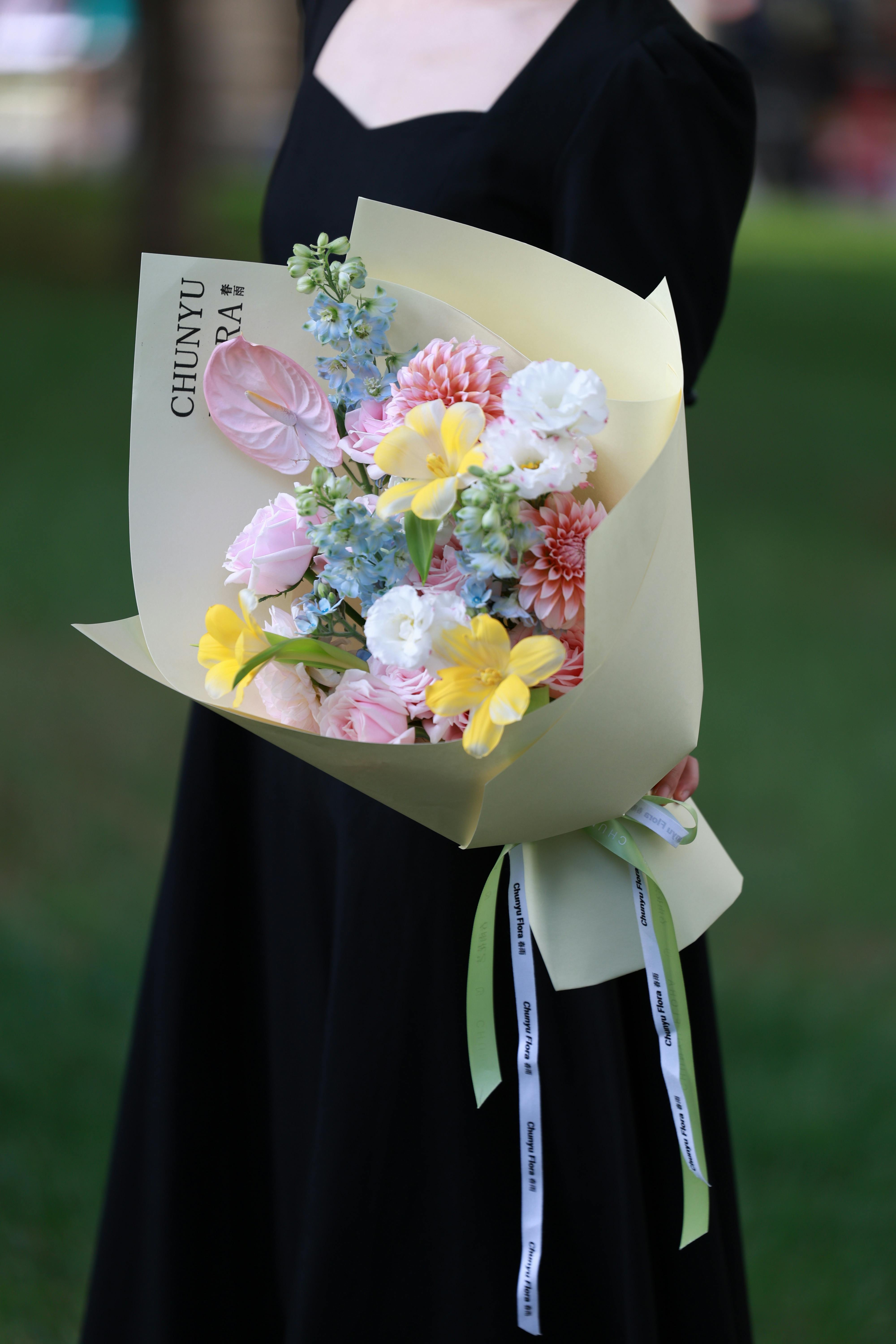 A woman in a black dress holds a colorful bouquet with yellow, pink, and white flowers.