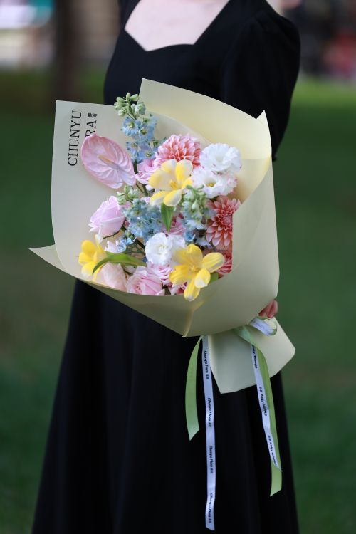 Free A woman in a black dress holds a colorful bouquet with yellow, pink, and white flowers. Stock Photo