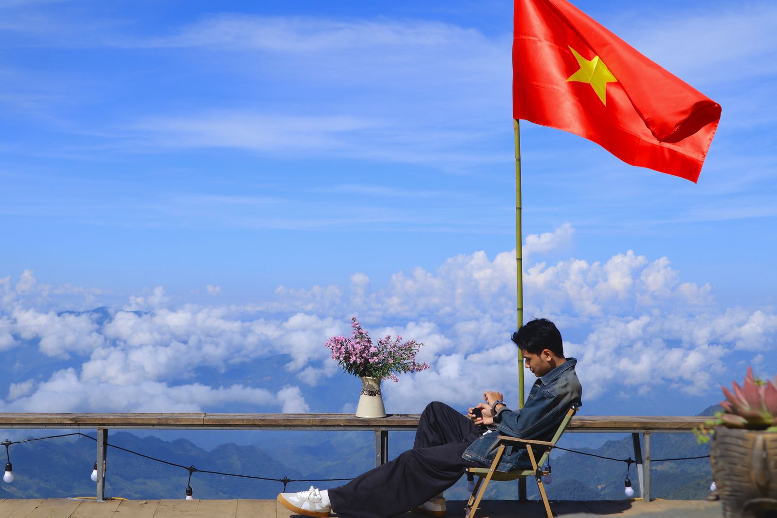 Man sits under the Vietnamese flag with stunning mountain view in the background.