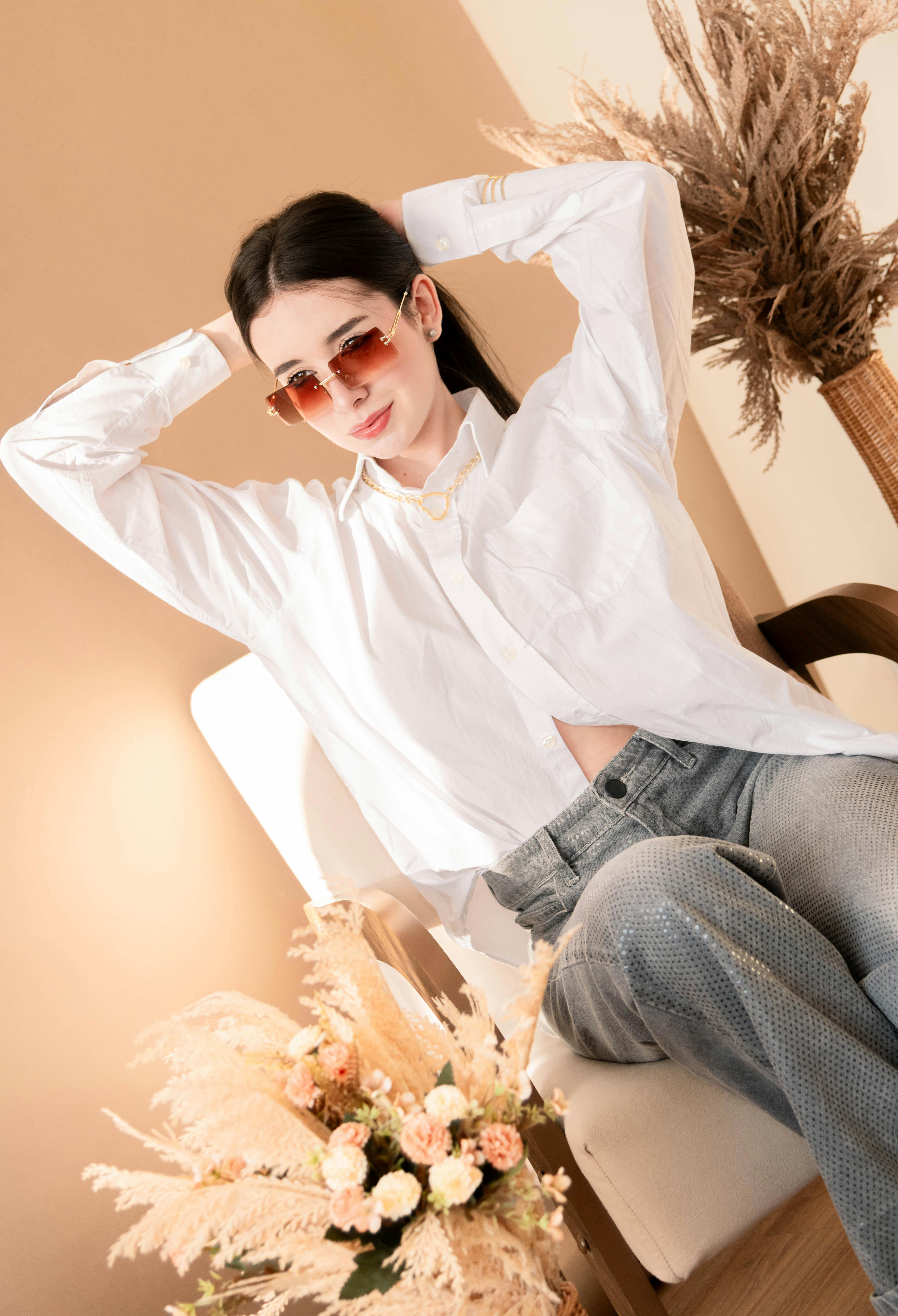 grátis Mulher moderna em traje casual e óculos de sol sentada em um ambiente interno, cercada por uma decoração típica dos pampas. Foto profissional