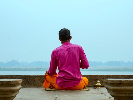A man in colorful attire meditates by the river, enjoying peaceful solitude.