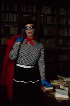 Chic woman in striped outfit in vintage library holding books, exuding fashion elegance.