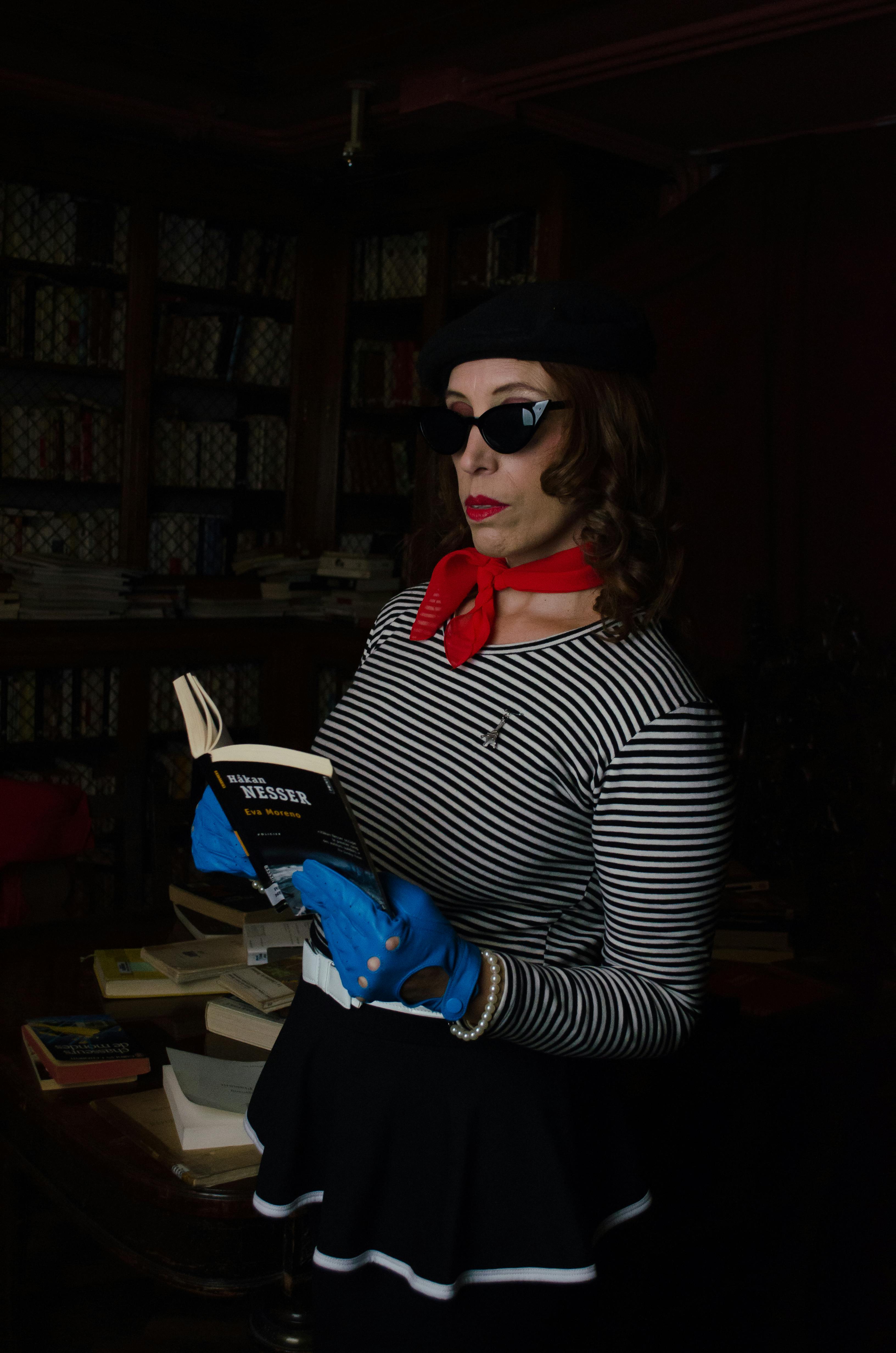 Elegant woman in vintage attire reads a book in a dark, cozy library setting.