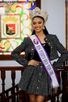 Teen girl wearing a crown and sash posing inside a beautiful room.