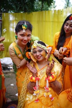 Joyful Indian pre-wedding ceremony with women in traditional attire, adorned in floral jewelry and henna designs.