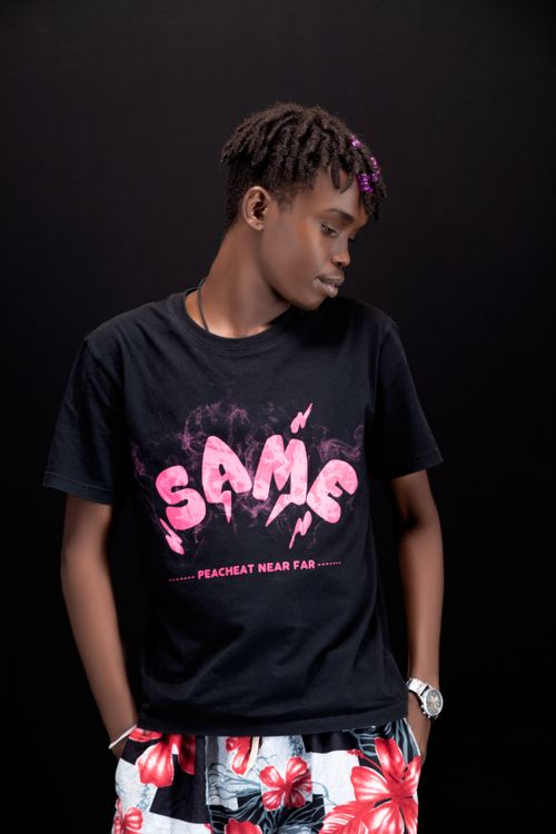 Free Young man in a stylish outfit, vibrant floral shorts, and graphic tee posing against a black background. Stock Photo