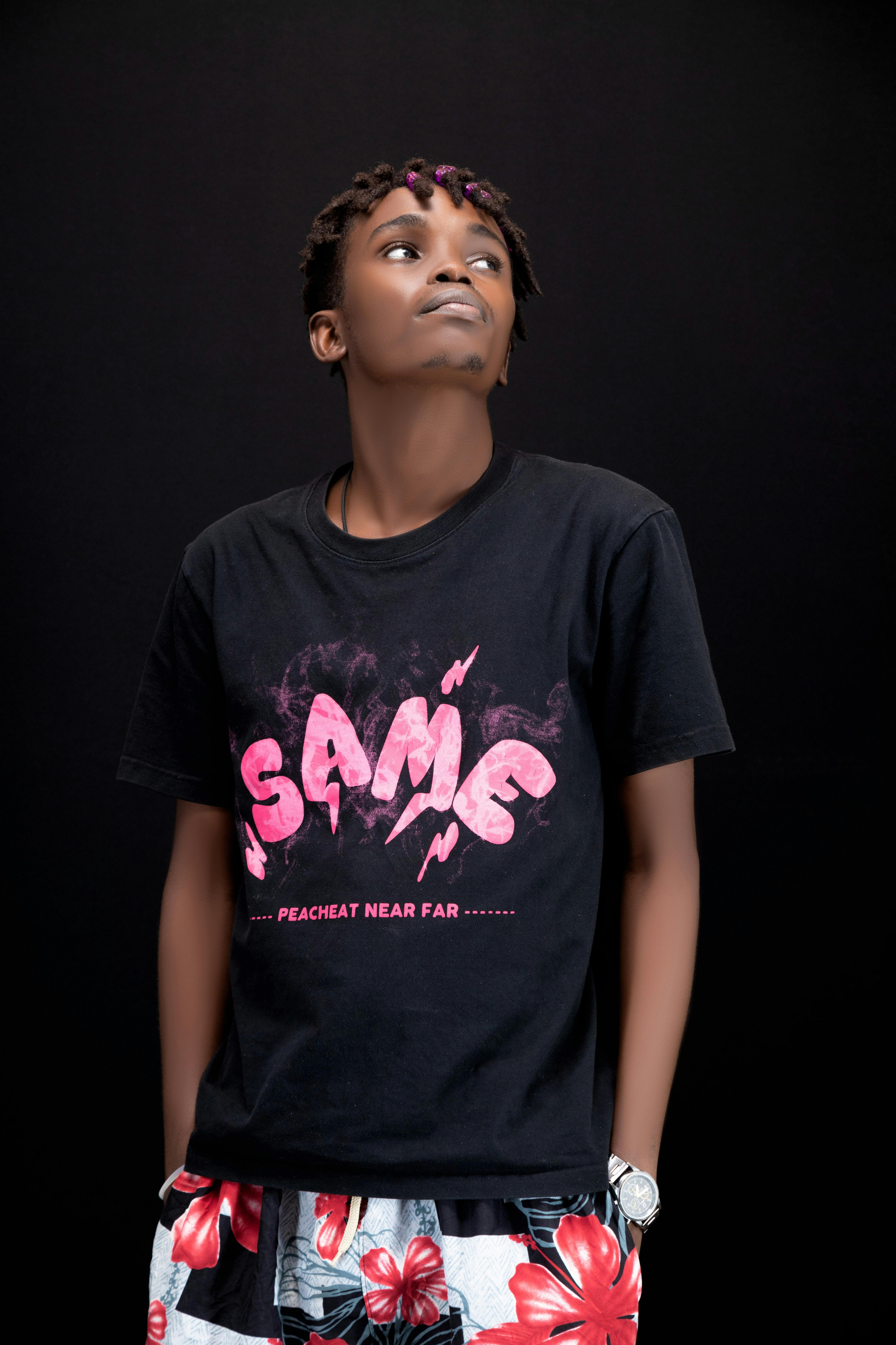 Portrait of a young adult wearing a graphic tee and floral shorts against a dark background.