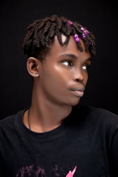A striking portrait of a stylish person with beaded dreadlocks on a dark background.