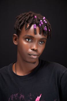 Portrait of a young man with dreadlocks and purple beads, against a dark background.