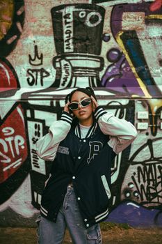 Stylish individual poses confidently in front of vibrant street art mural.