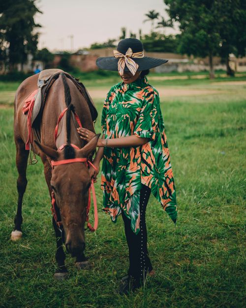 Free A woman in a colorful dress interacting with a horse in a lush green field in Zaria, Nigeria. Stock Photo