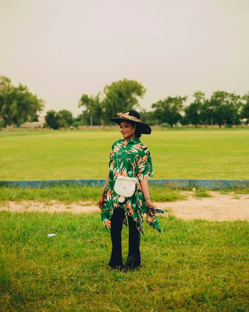 Free Fashionable woman in floral dress and straw hat standing in a grassy field. Stock Photo