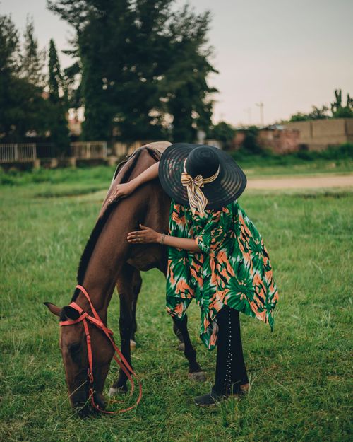 Free A woman in a stylish outfit embraces a horse in a grassy field. Stock Photo