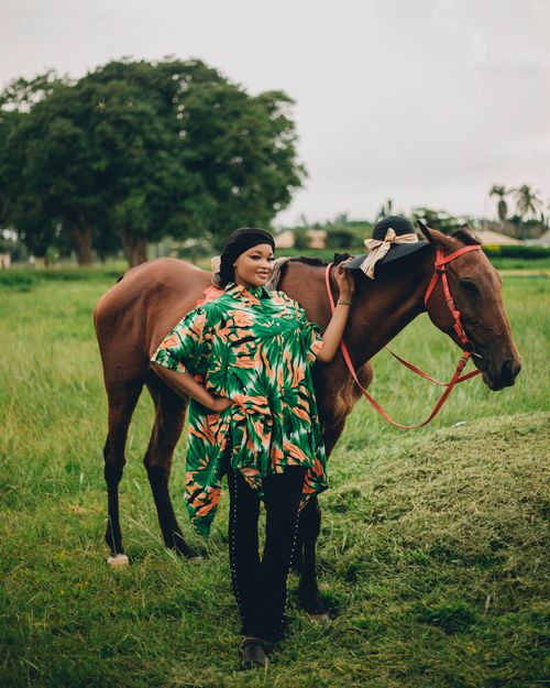 Free A woman in vibrant attire posing with a horse in a lush green field, exuding calmness. Stock Photo