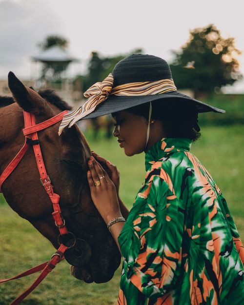 Free A stylish woman in a hat shares a serene moment with a horse in a tranquil outdoor setting. Stock Photo