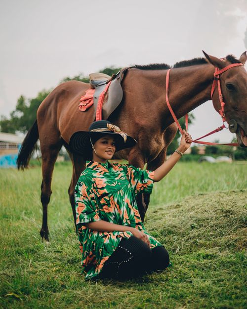 Free A woman in a colorful dress smiling while kneeling next to a horse in a grassy field. Stock Photo