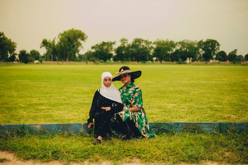 Free Two women sitting in a park wearing colorful outfits, enjoying a peaceful day outdoors. Stock Photo