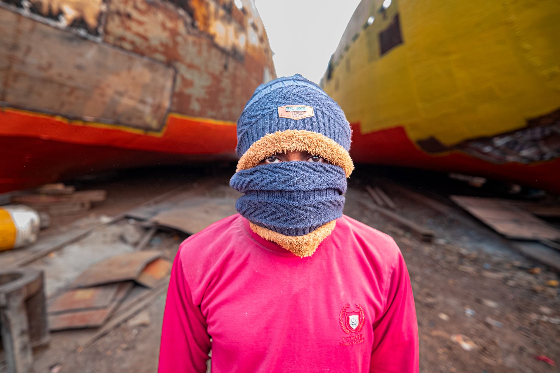 A worker stands at a shipyard, bundled in warm clothing between two large ships.