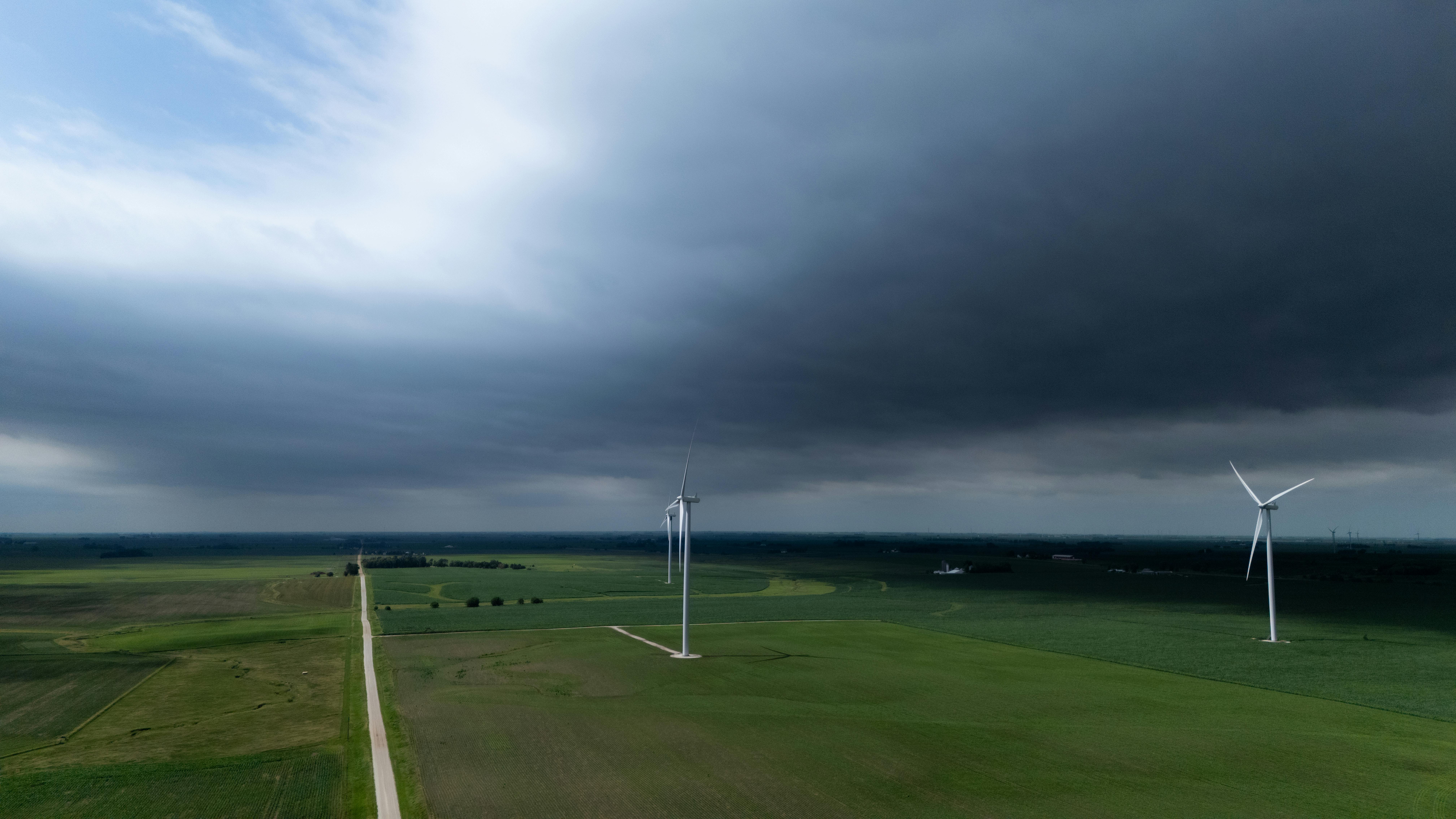 무료 폭풍우가 치는 하늘 아래 광활한 푸른 들판 위에 있는 풍력 터빈의 공중 촬영. 스톡 사진