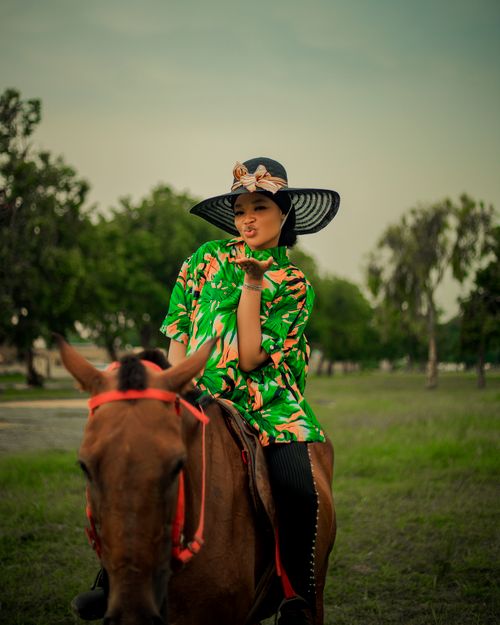 Free Woman in striking outfit and hat posing playfully on a horse outdoors. Stock Photo