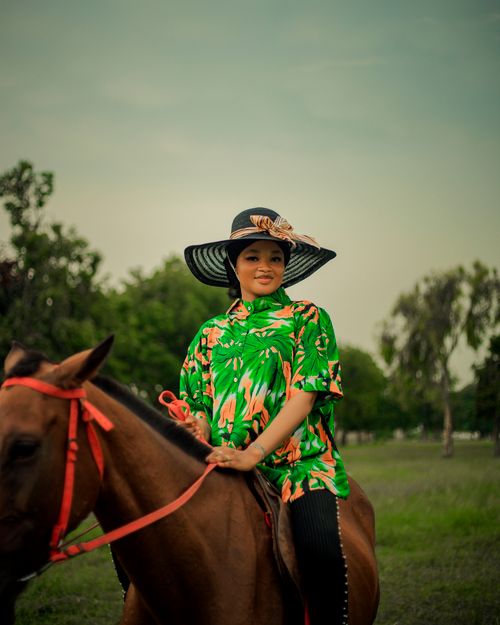 Free Stylish woman on horse wearing a large hat with floral shirt outdoors. Stock Photo