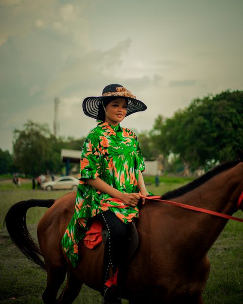 Free Woman in a colorful floral dress riding a horse outdoors on a cloudy day. Stock Photo
