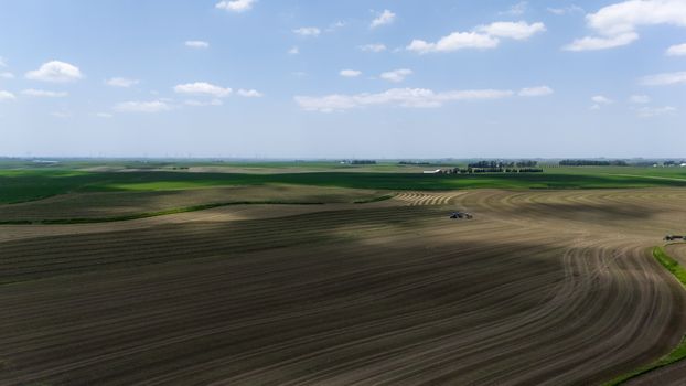 Aerial view of expansive farm fields with a tractor during summer harvest.